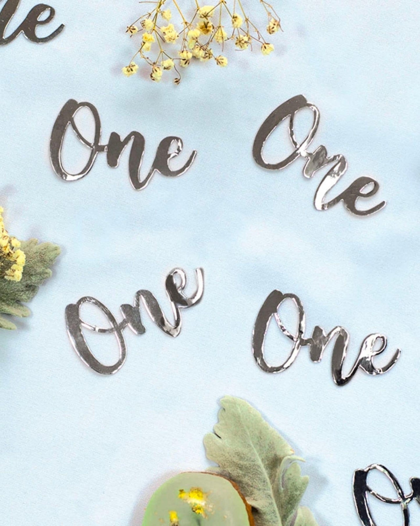 Shiny silver "One" text pieces scattered among delicate flowers and soft green leaves on a light blue background.