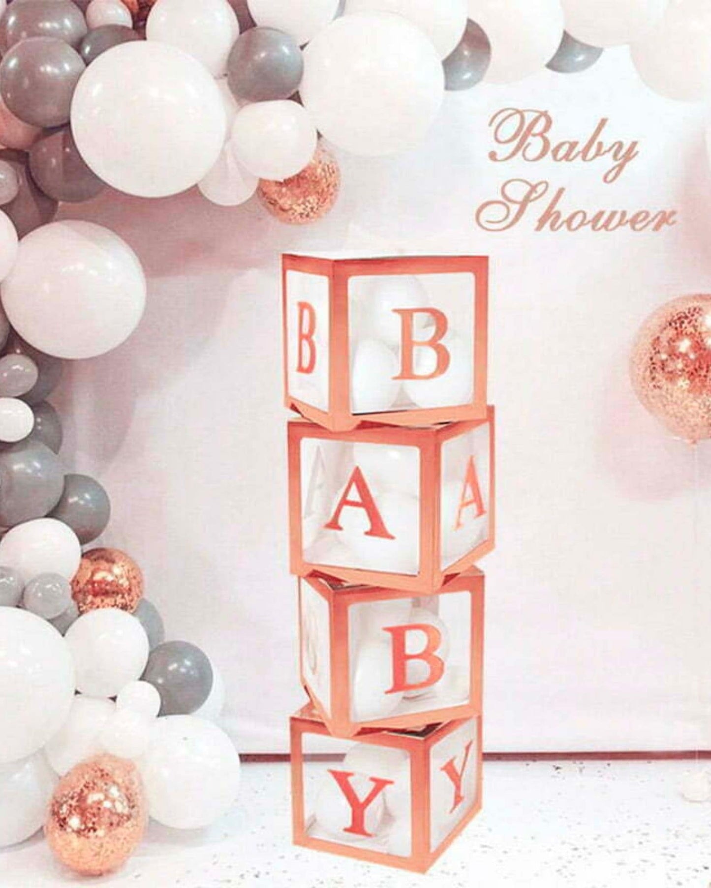 Colorful balloons in shades of white, gray, and copper surround stacked blocks spelling "BABY" for a celebration backdrop.