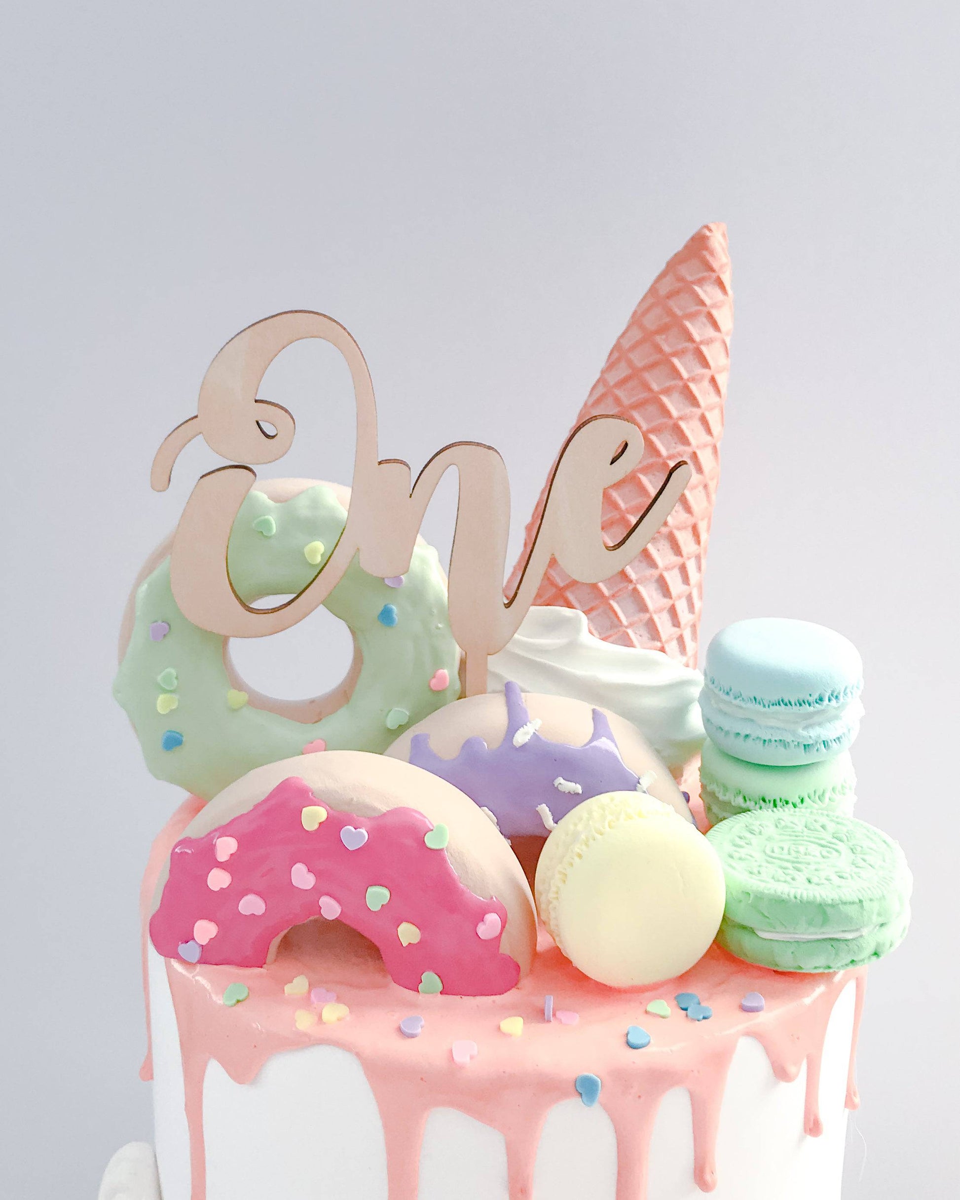 A colorful cake topper featuring the word "One" alongside vibrant, whimsical treats and an ice cream cone.