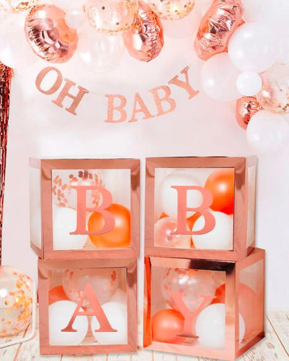 Rose gold and white balloons arranged with letters spelling "BABY" in decorative boxes, under a banner reading "OH BABY."