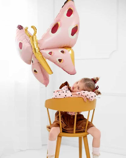 A child in a brown dress rests on a yellow chair, gazing at a large pink butterfly floating above.