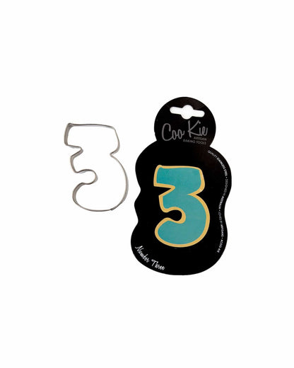 A metal cutter shaped like the number three, displayed on a black backing with colorful accents.