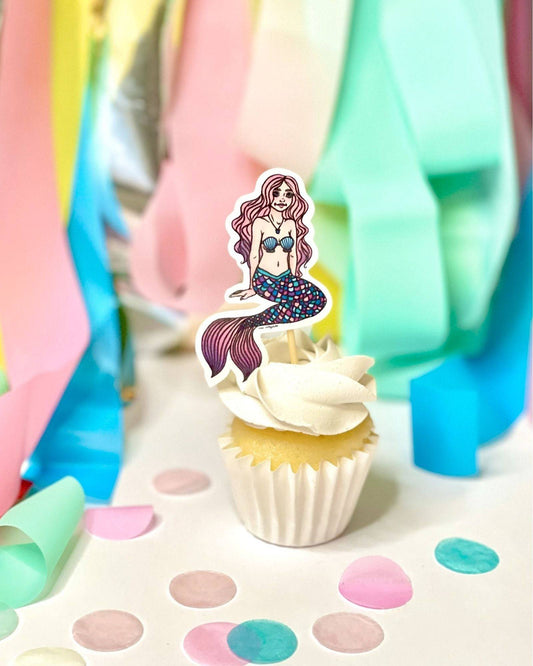 A whimsical cupcake topped with a mermaid decoration, surrounded by colorful confetti and pastel streamers.