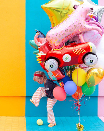 A child in striped pants plays with colorful balloons against a vibrant backdrop of bold, bright colors.