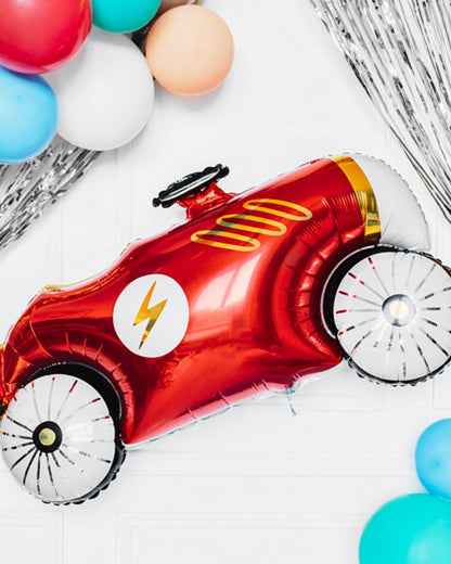 A shiny red balloon shaped like a vintage race car, with decorative wheels and surrounded by colorful balloons.