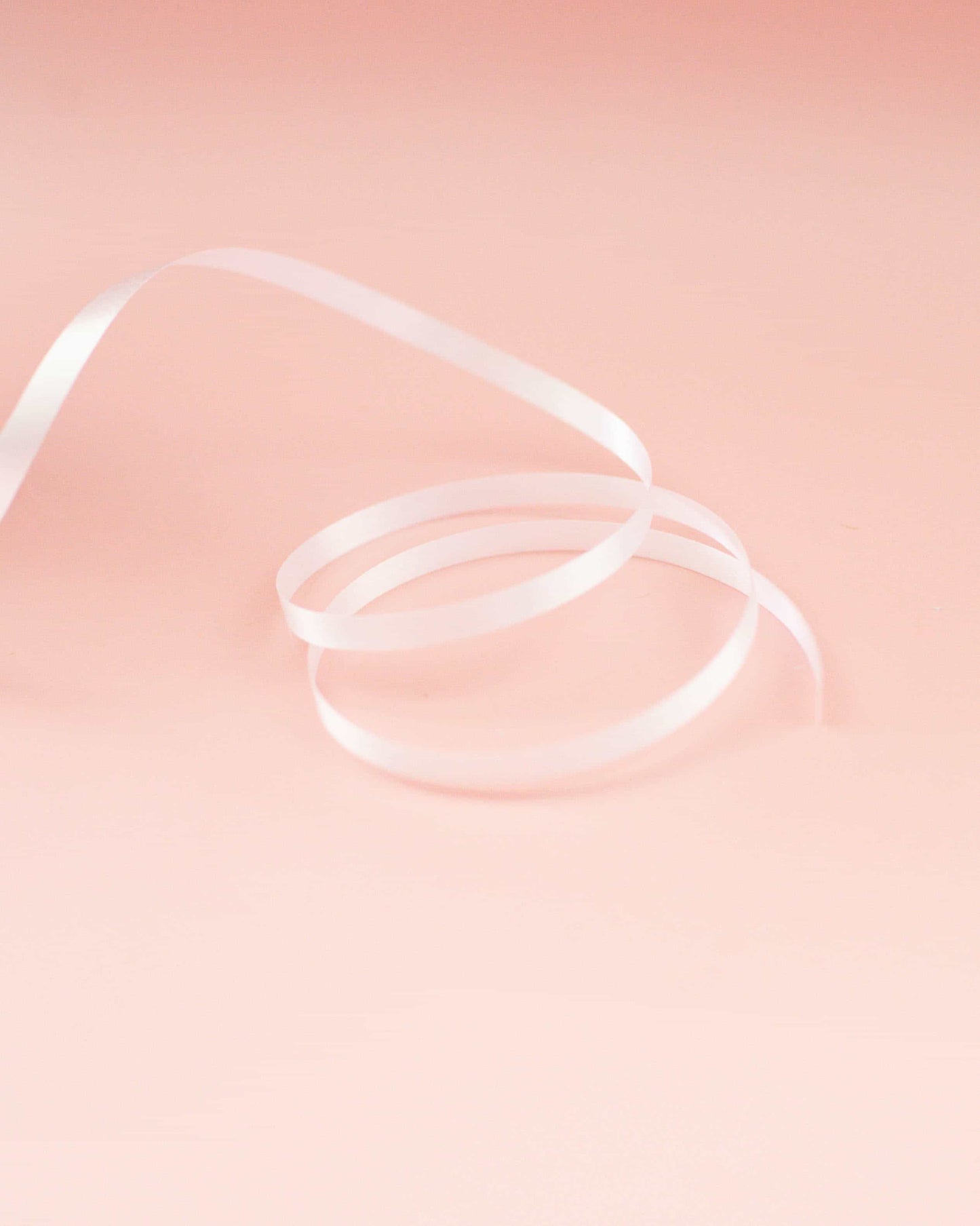 White curling ribbon arranged in loops against a soft pink background, creating a delicate and elegant appearance.