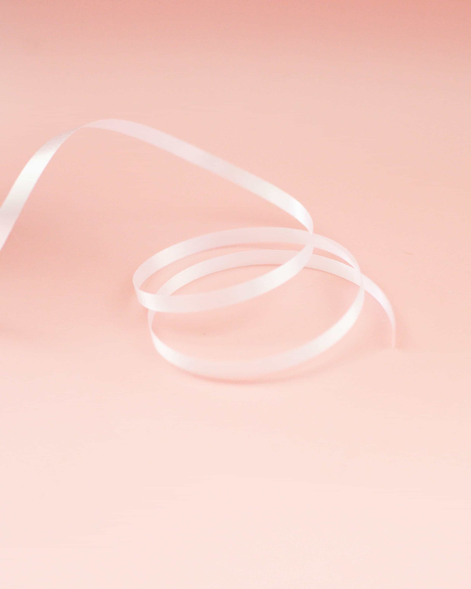 White curling ribbon arranged in loops against a soft pink background, creating a delicate and elegant appearance.