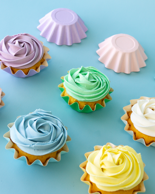 Colorful piped frosting swirls atop baked treats, arranged on a light blue background with pastel wrappers.