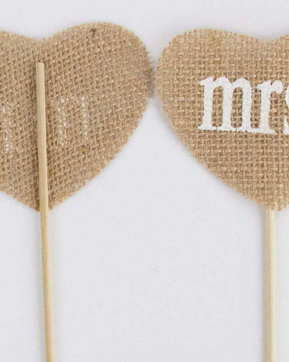 Two burlap heart shapes on sticks, one printed with "mr." and the other with "mrs." against a plain background.