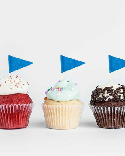 Three colorful cupcakes topped with frosting and blue glitter flags, arranged against a light background.