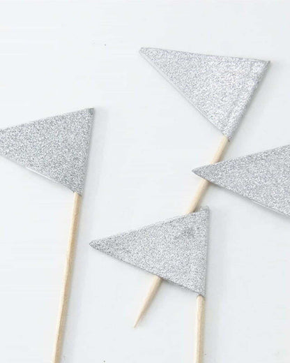 Four small silver glitter triangular shapes attached to wooden sticks on a light background.