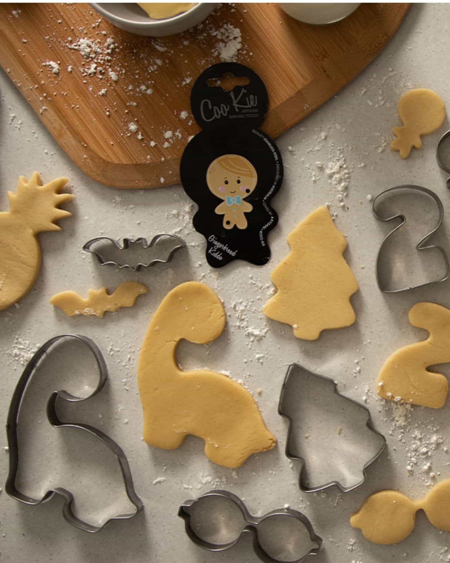 Assorted cookie shapes, including a tree and bat, scattered on a floured surface with a wooden board in the background.