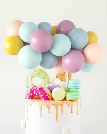 Colorful balloons adorn a whimsical cake topped with donuts, macarons, and an ice cream cone.