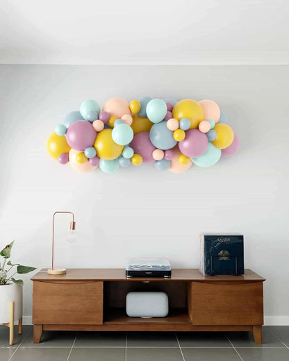 Colorful balloon arrangement featuring pastel shades, mounted on a wall above a wooden console with decor elements.