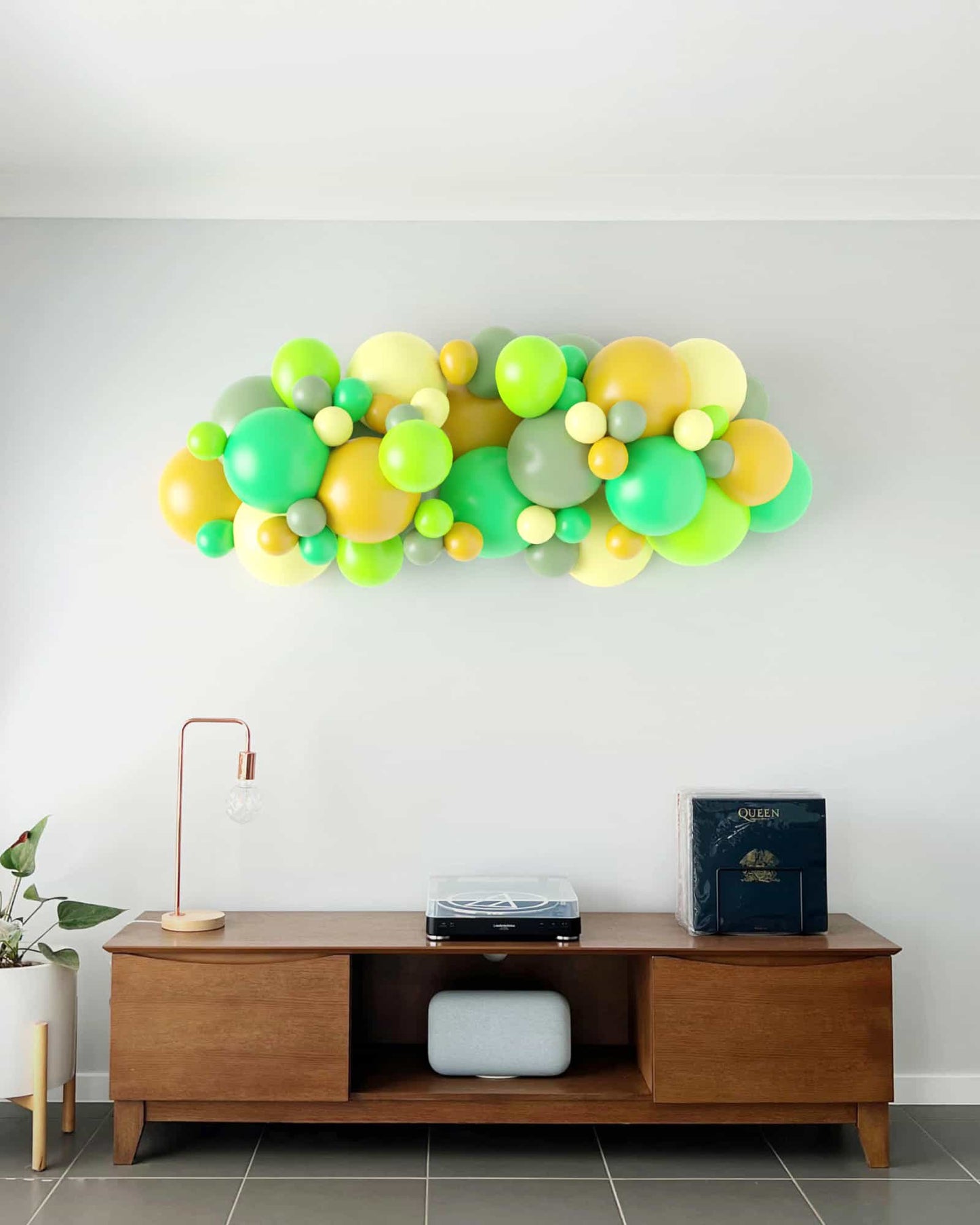 A vibrant garland of green and yellow balloons adorns a wall above a wooden console table with decor elements.