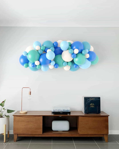 A vibrant garland of balloons in shades of blue and green, elegantly arranged against a light wall.