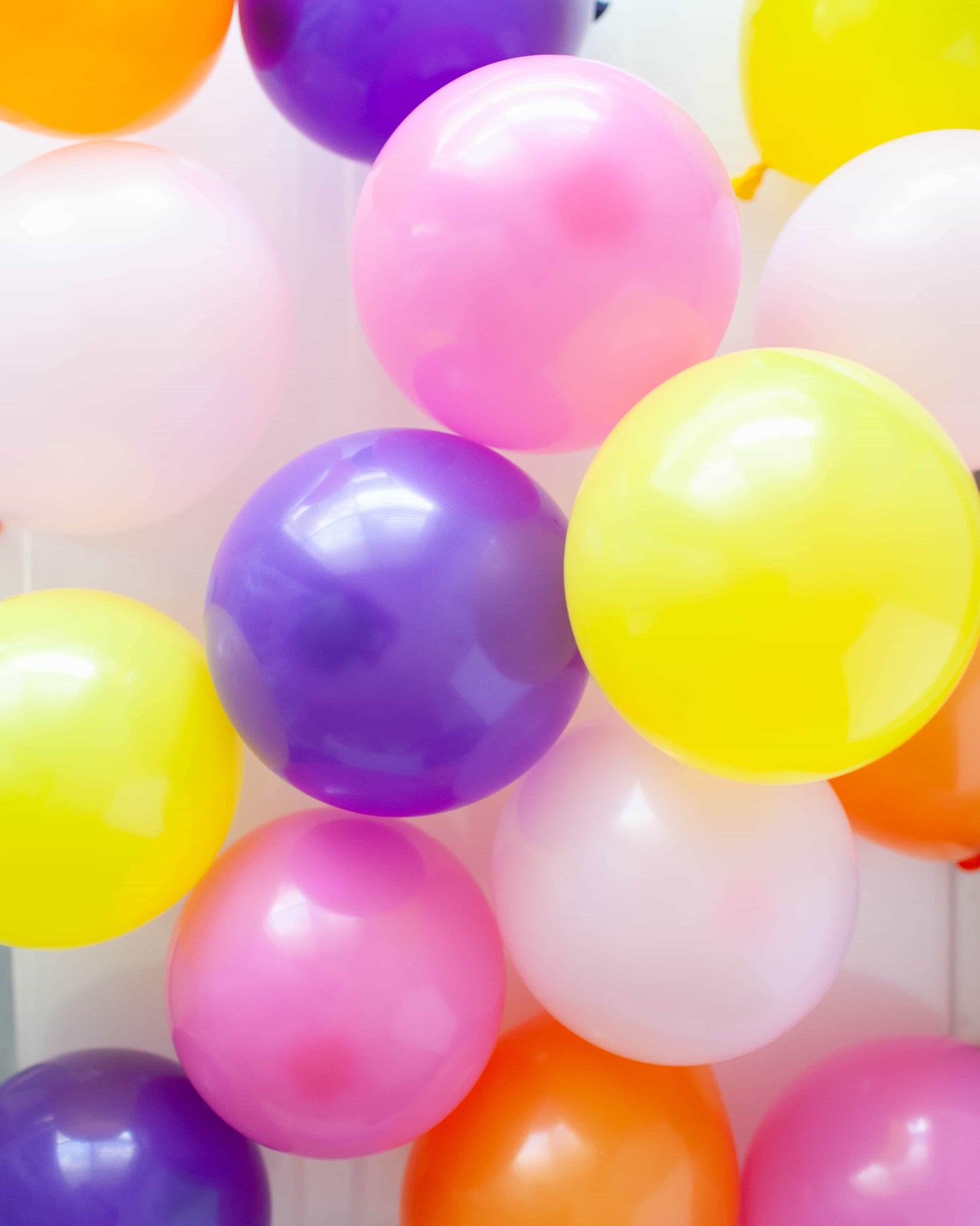 A vibrant cluster of colorful balloons in shades of pink, purple, yellow, orange, and white against a light background.