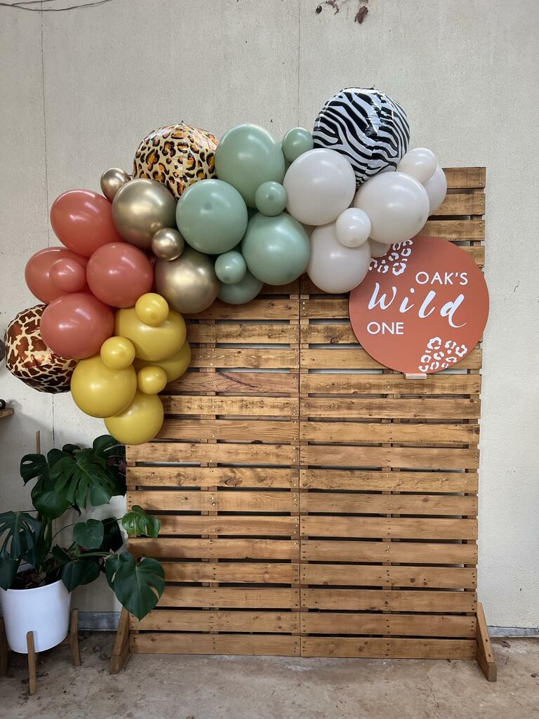 Colorful balloon arrangement with animal prints and a wooden backdrop, celebrating a child's first birthday.