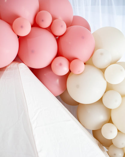 A cluster of soft pink and cream balloons elegantly draping over a white surface, creating a playful and festive atmosphere.