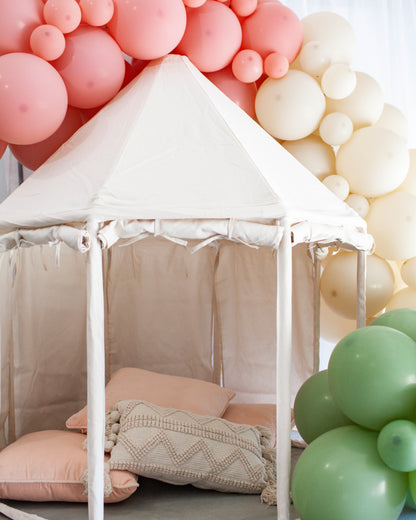 A cozy tent adorned with soft pillows and vibrant pastel balloons in pink, cream, and green hues.