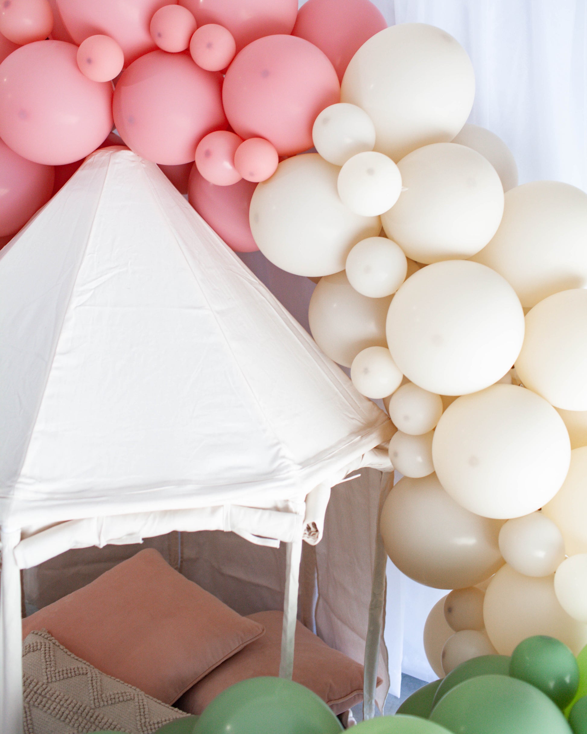 A whimsical arrangement of pink and cream balloons surrounding a cozy, fabric-covered nook with soft pillows.