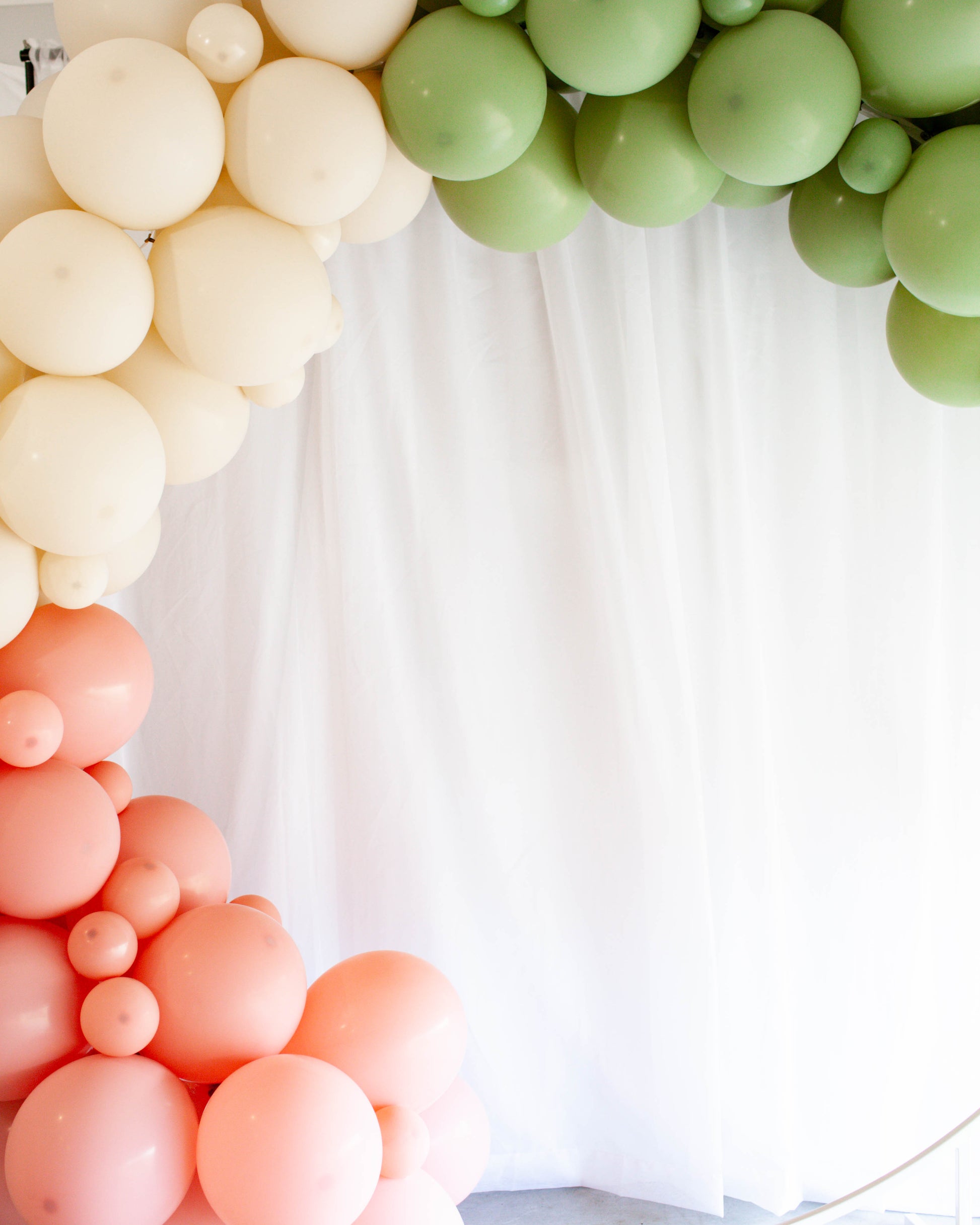 A colorful balloon arch featuring soft pink, beige, and green hues against a light backdrop.