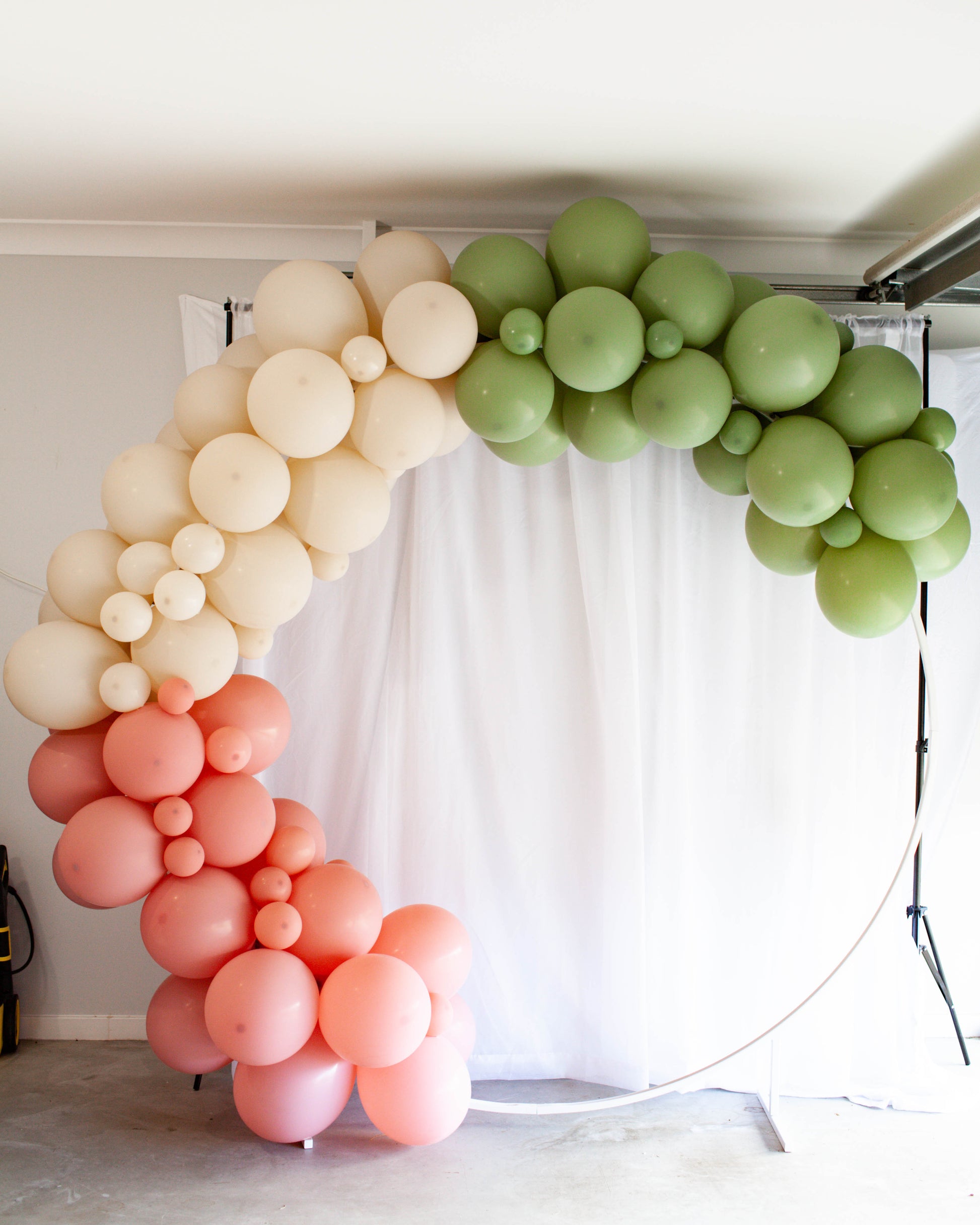 A colorful arch made of balloons in shades of pink, cream, and green against a white backdrop.