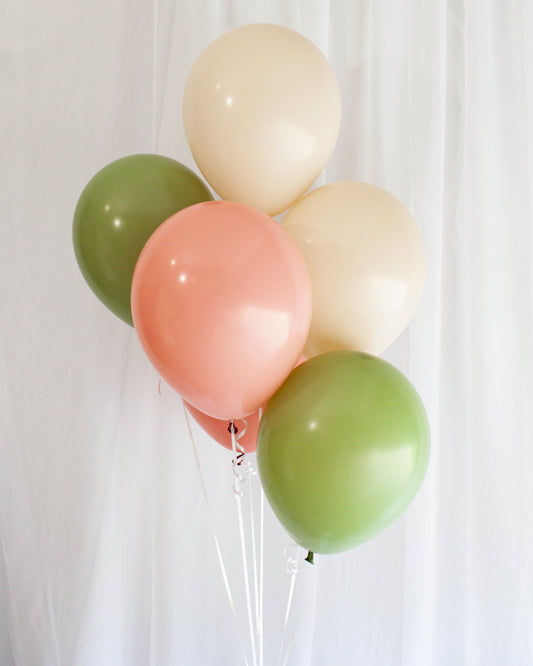 A cluster of pastel balloons in pink, green, and cream against a soft white background.