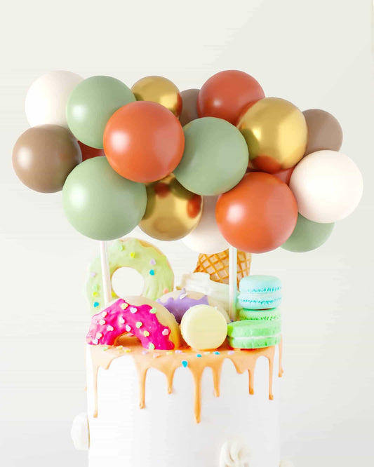 Colorful balloon topper with playful sweets, including donuts and macarons, atop a drizzled cake.