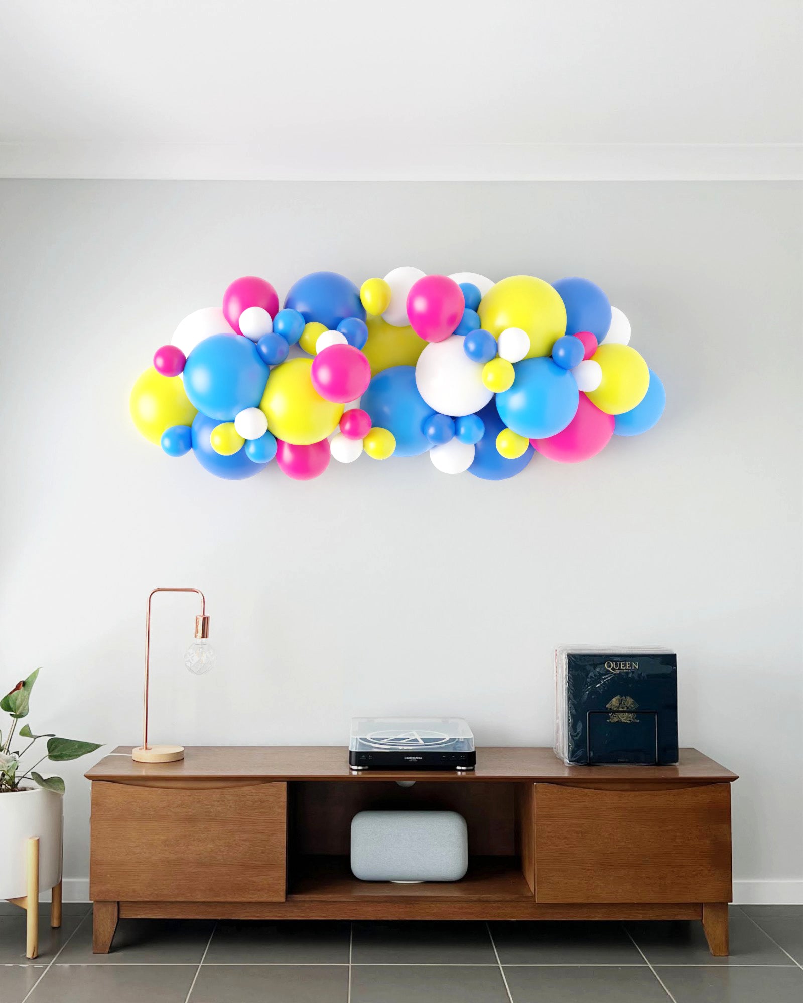 Colorful balloon garland in pink, blue, yellow, and white, displayed above a wooden console with decorative elements.