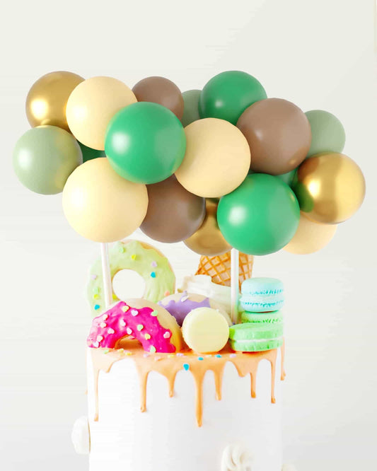 A colorful arrangement of balloons atop a cake decorated with donuts, macarons, and an ice cream cone.