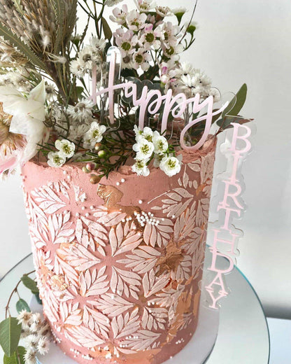 Pink layered creation adorned with delicate flowers and gold leaf, featuring a "Happy Birthday" topper.