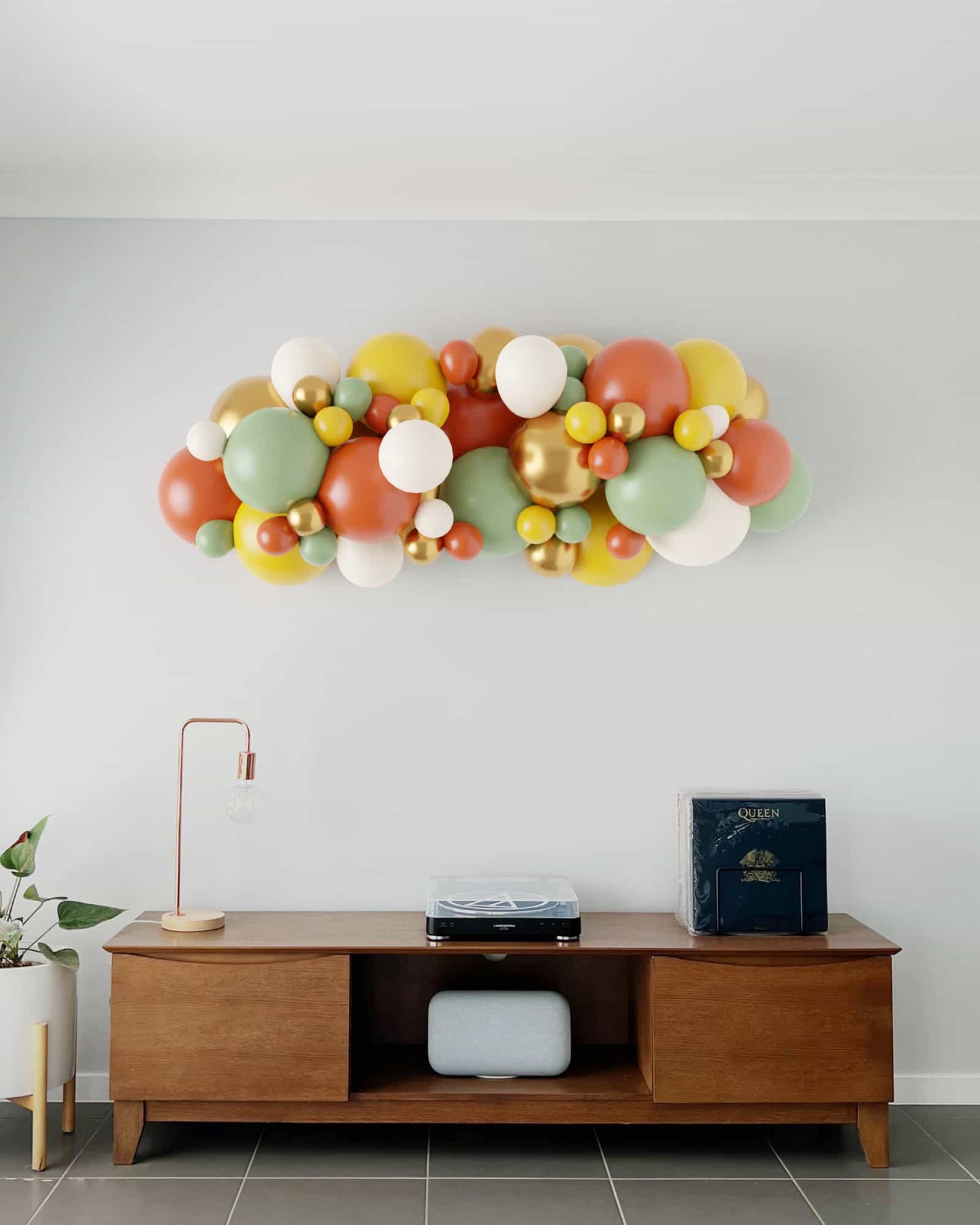 Colorful balloon garland featuring greens, oranges, yellows, and whites, mounted above a wooden console table.