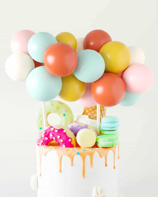 A vibrant cake topped with colorful balloons and playful treats like donuts, macarons, and an ice cream cone.