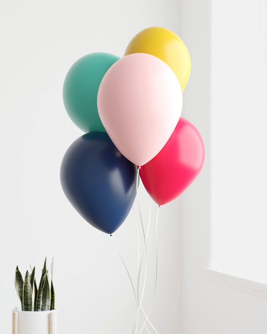 A colorful bunch of balloons in teal, pink, yellow, navy, and red, with a potted plant in the background.