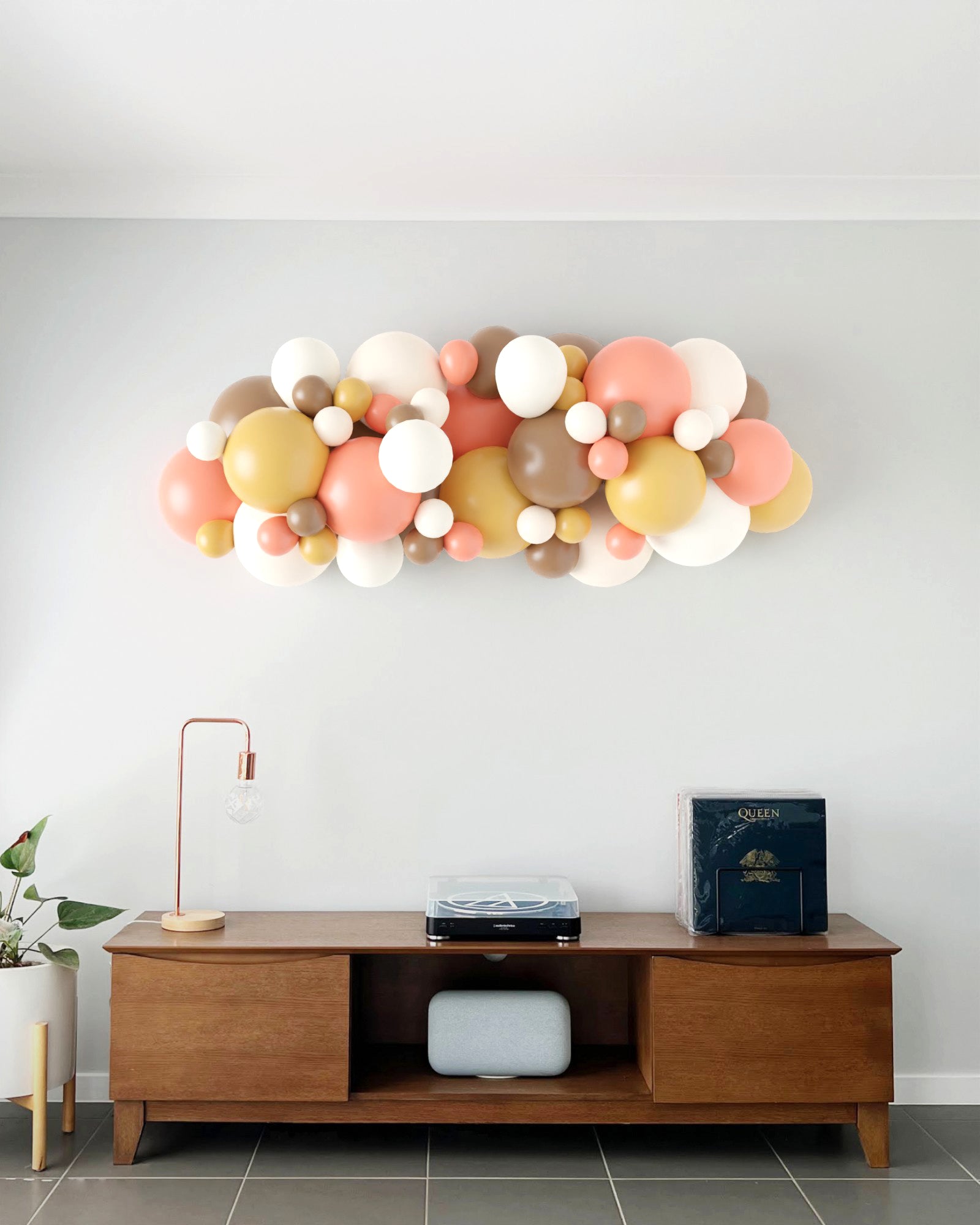 A colorful balloon garland featuring soft pinks, whites, browns, and yellows, displayed against a light wall.