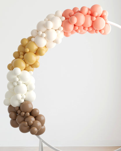 A colorful arch made of various-sized balloons in shades of peach, cream, gold, and brown against a neutral background.
