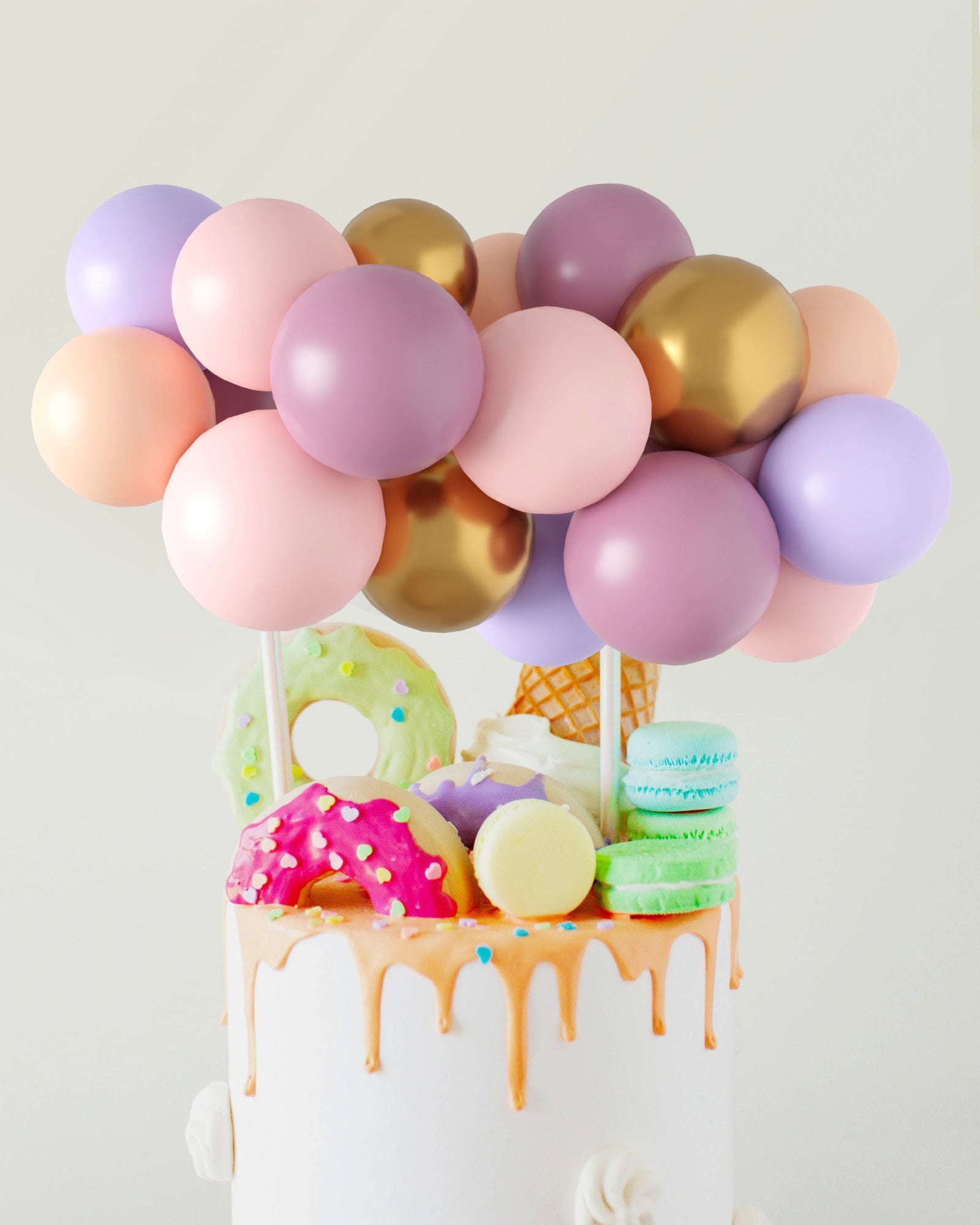 Colorful balloons in pastel shades top a whimsical cake adorned with playful sweets and dripping icing.