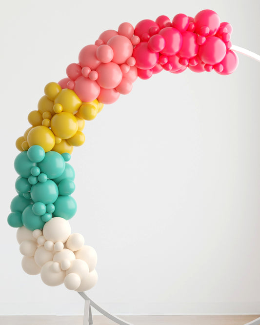 Colorful balloon garland in pink, yellow, teal, and white, arching gracefully against a light background.