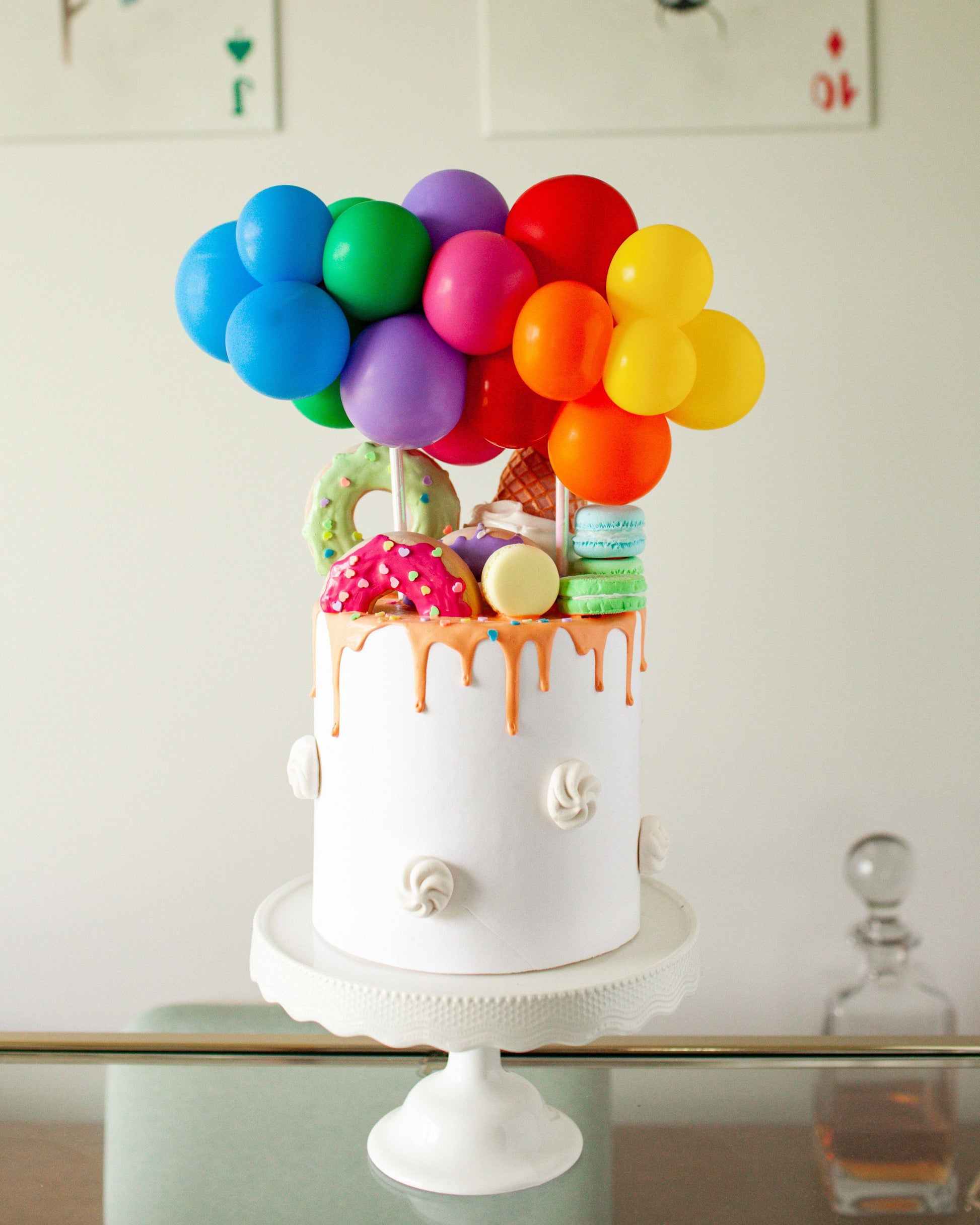 A colorful cake topped with vibrant balloons and assorted sweet treats like donuts and macarons.