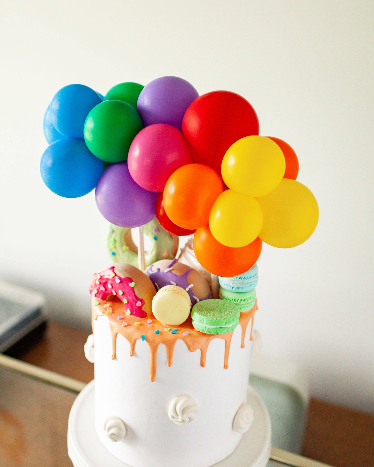 Colorful balloons in various shades hover above a cake adorned with vibrant sprinkles and an assortment of sweets.