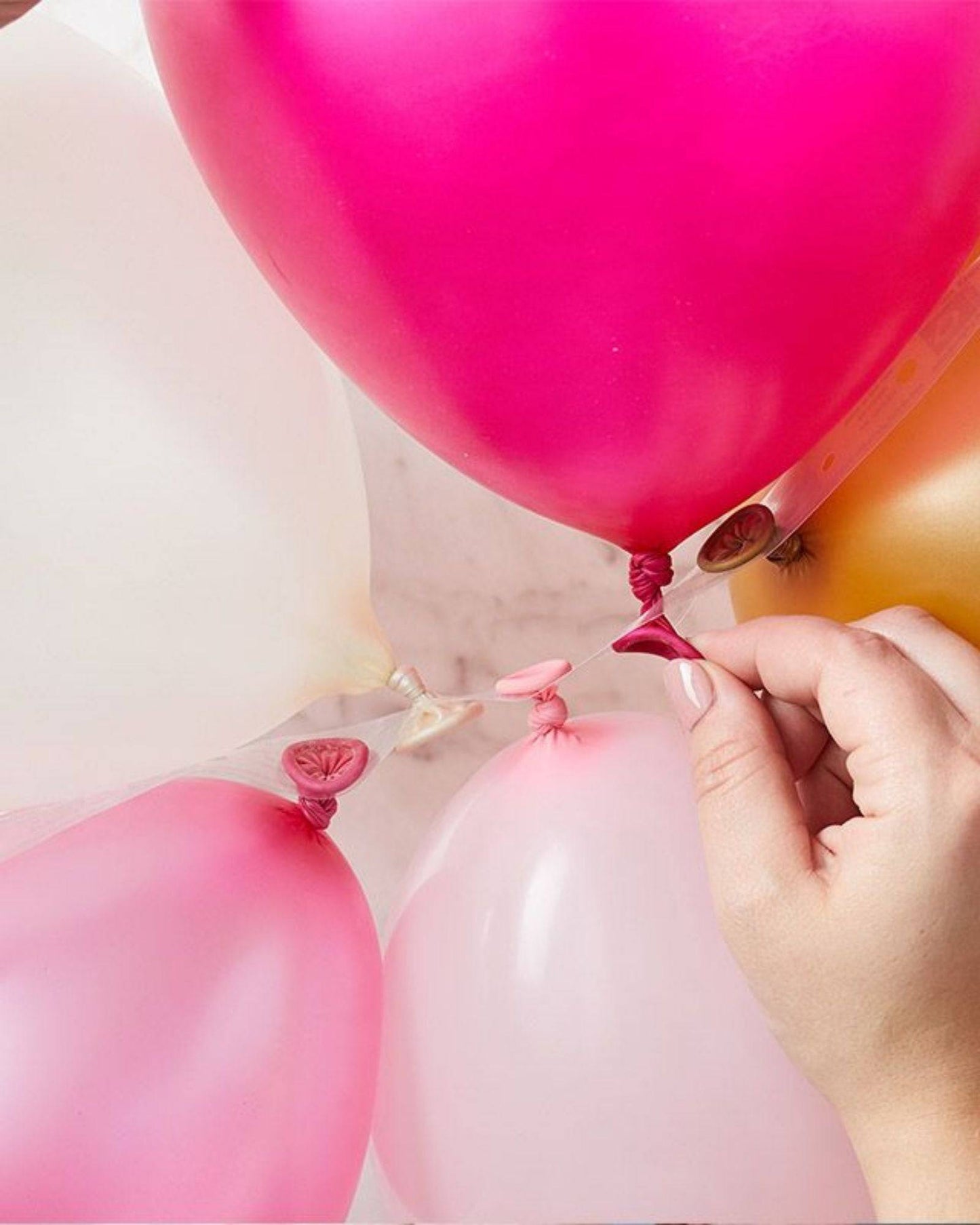 A hand attaching colorful balloons of various shades together with a decorative strip.