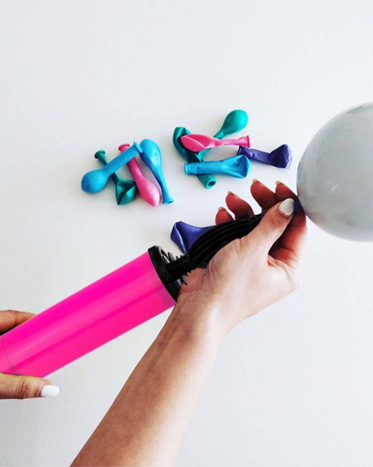 A person holds a bright pink pump while inflating a gray balloon, surrounded by colorful deflated balloons.