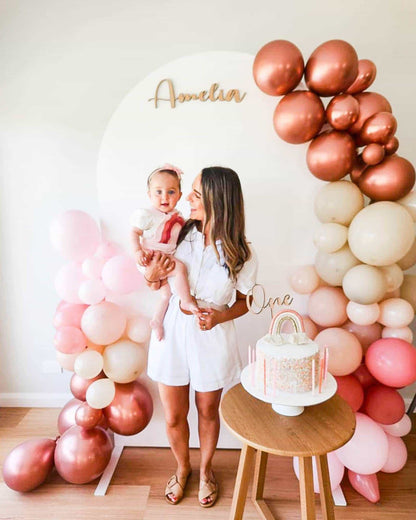 A joyful moment with a woman holding a baby, surrounded by pastel balloons and a beautifully decorated cake.