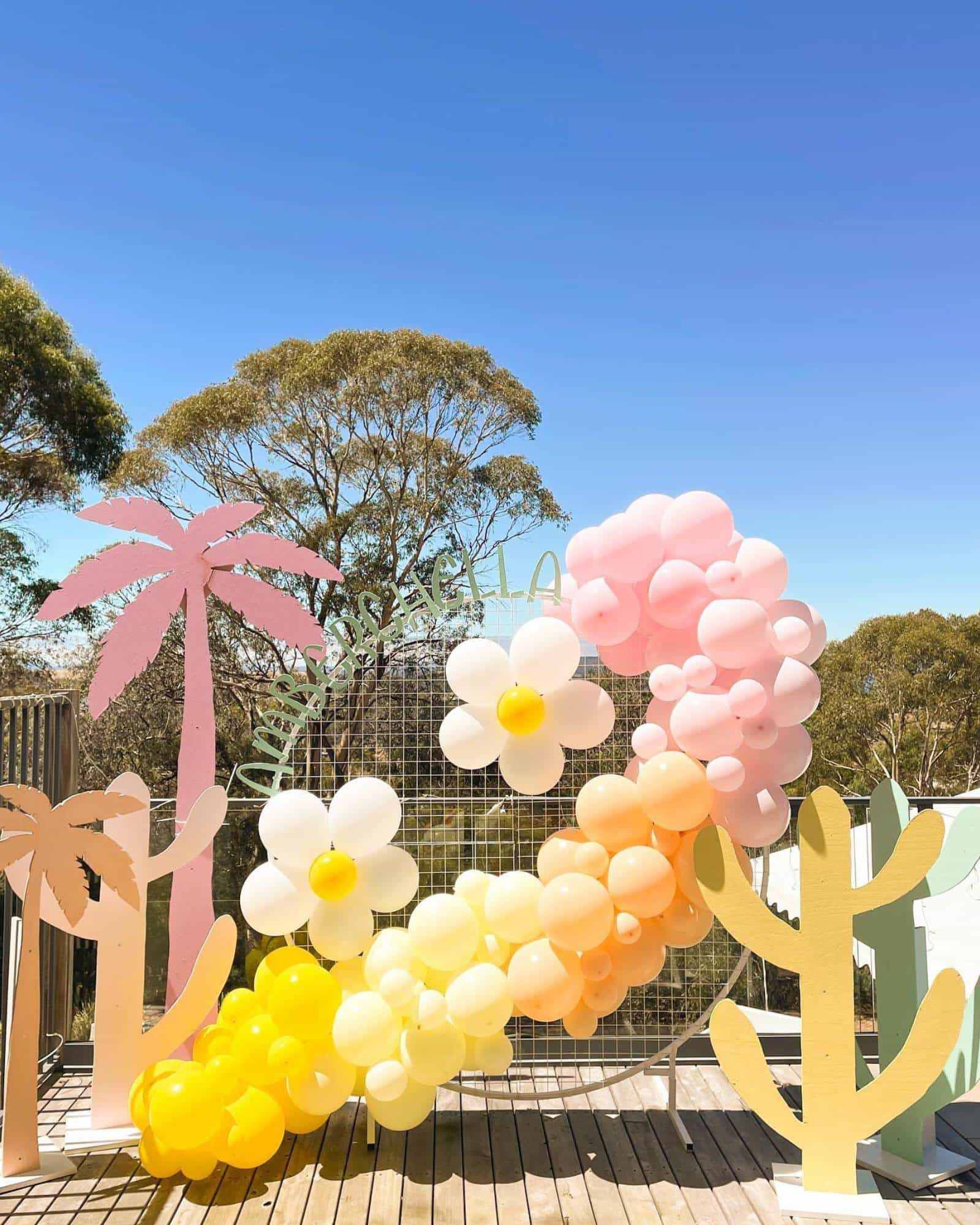 A colorful display of balloons and flower shapes, featuring pink, yellow, and white hues against a blue sky.