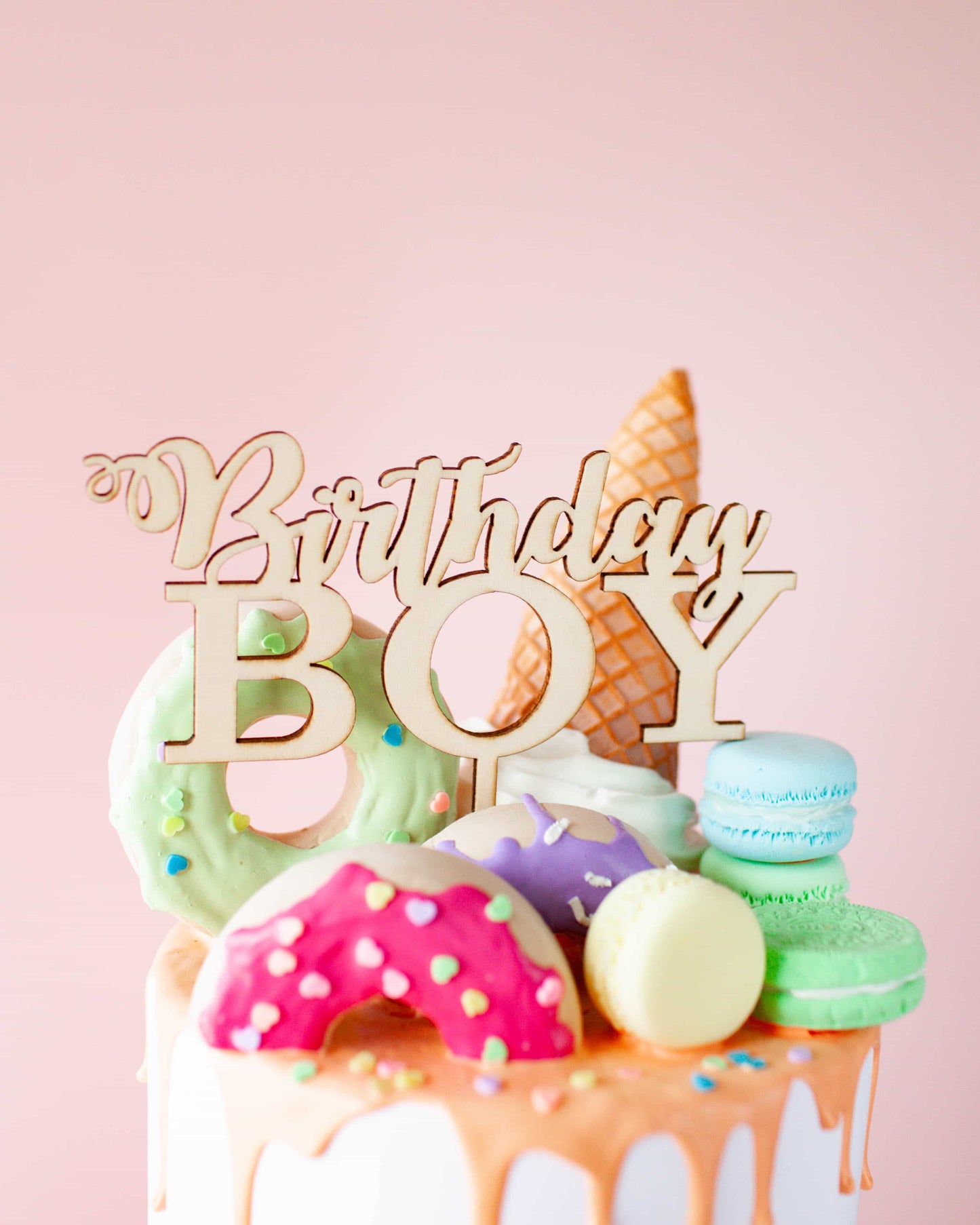 Wooden topper reads "Birthday Boy" atop a colorful cake adorned with playful, decorated treats and an ice cream cone.