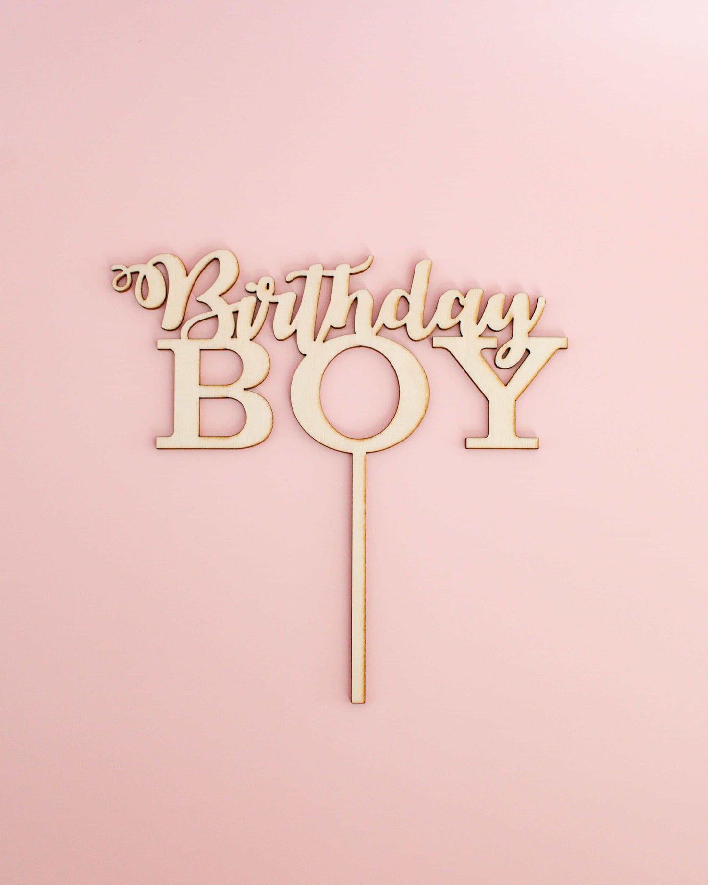 Wooden cake topper featuring the words "Birthday Boy" on a light pink background.