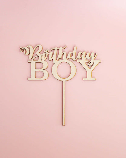 Wooden cake topper featuring the words "Birthday Boy" on a light pink background.