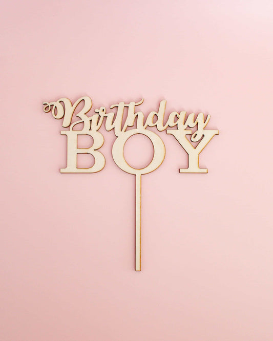 Wooden cake topper featuring the words "Birthday Boy" on a light pink background.