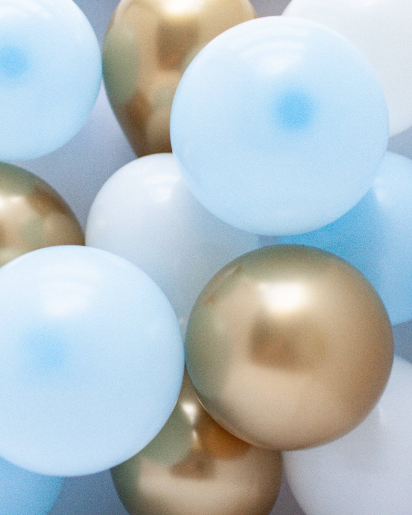 A mix of light blue, white, and shiny gold balloons clustered together, creating a festive and cheerful atmosphere.